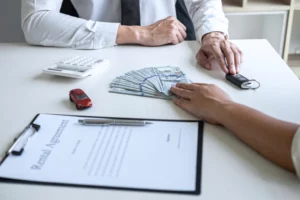Business meeting showing money, car keys, calculator and a rental-agreement clipboard on the table, illustrating a car-transaction scenario in a Chapter 13 bankruptcy context.