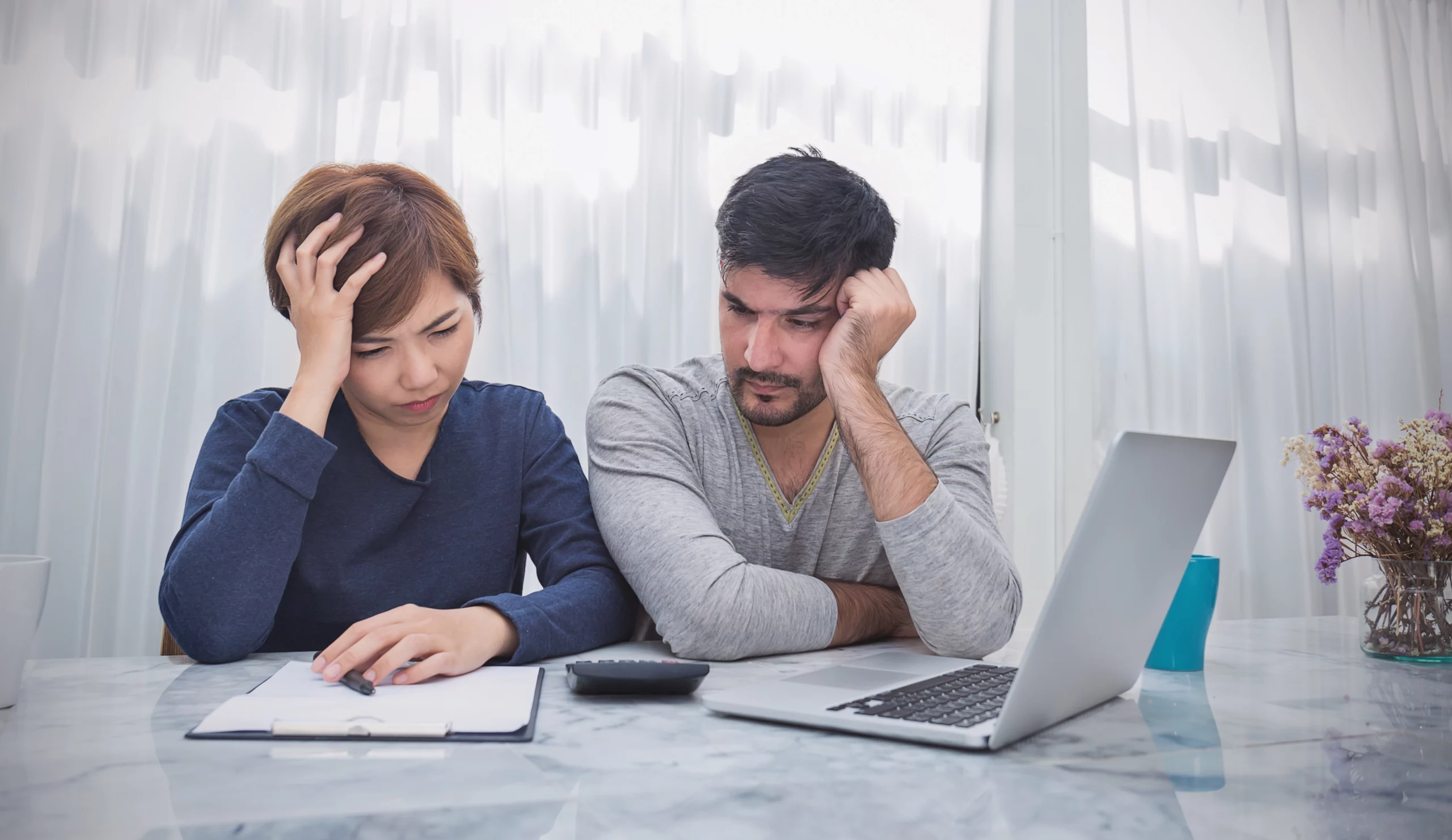 Couple stressed at table with papers, calculator and laptop, depicting financial decision-making and concern over one spouse filing bankruptcy in Florida.