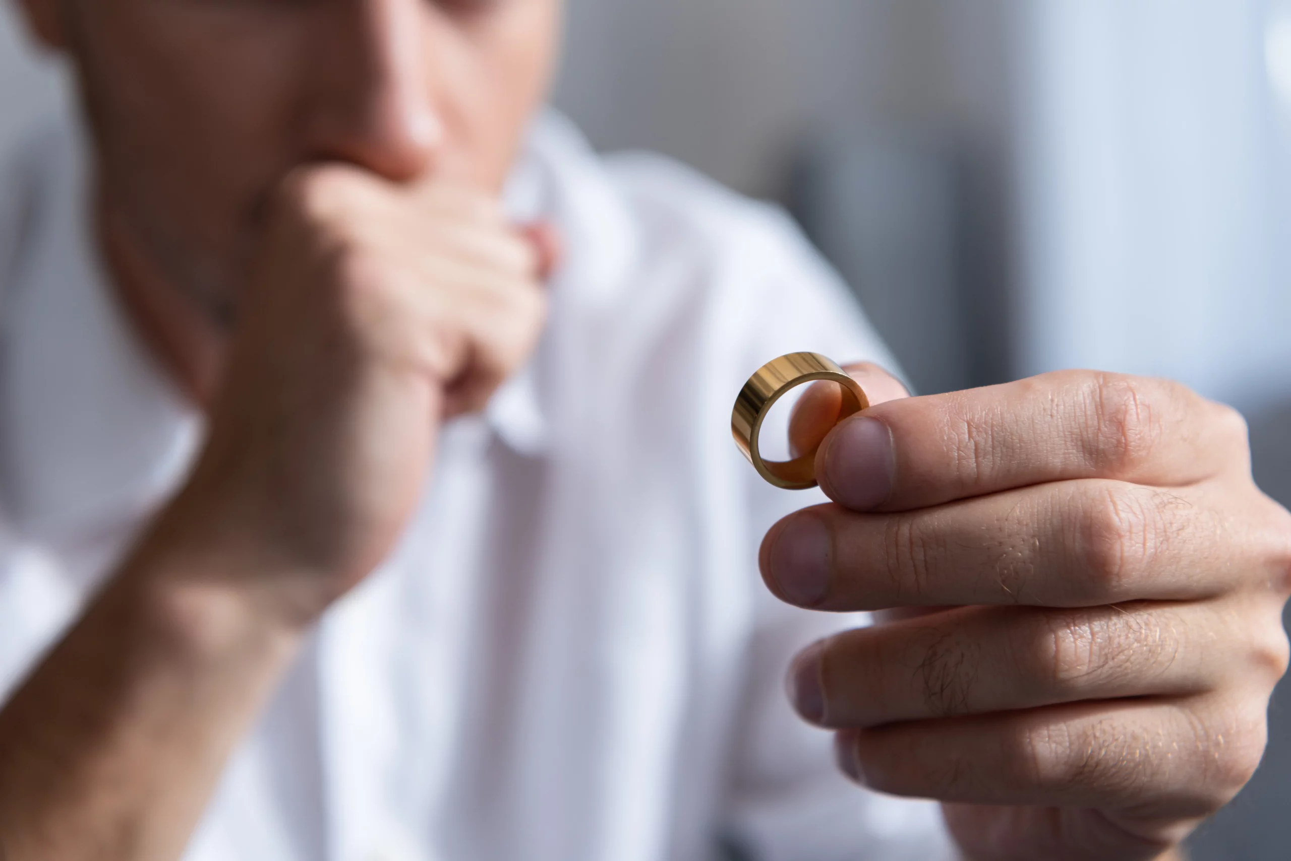 Person in white shirt holding a gold wedding ring thoughtfully, representing concerns about whether a wedding ring can be lost or exempted in a Florida bankruptcy